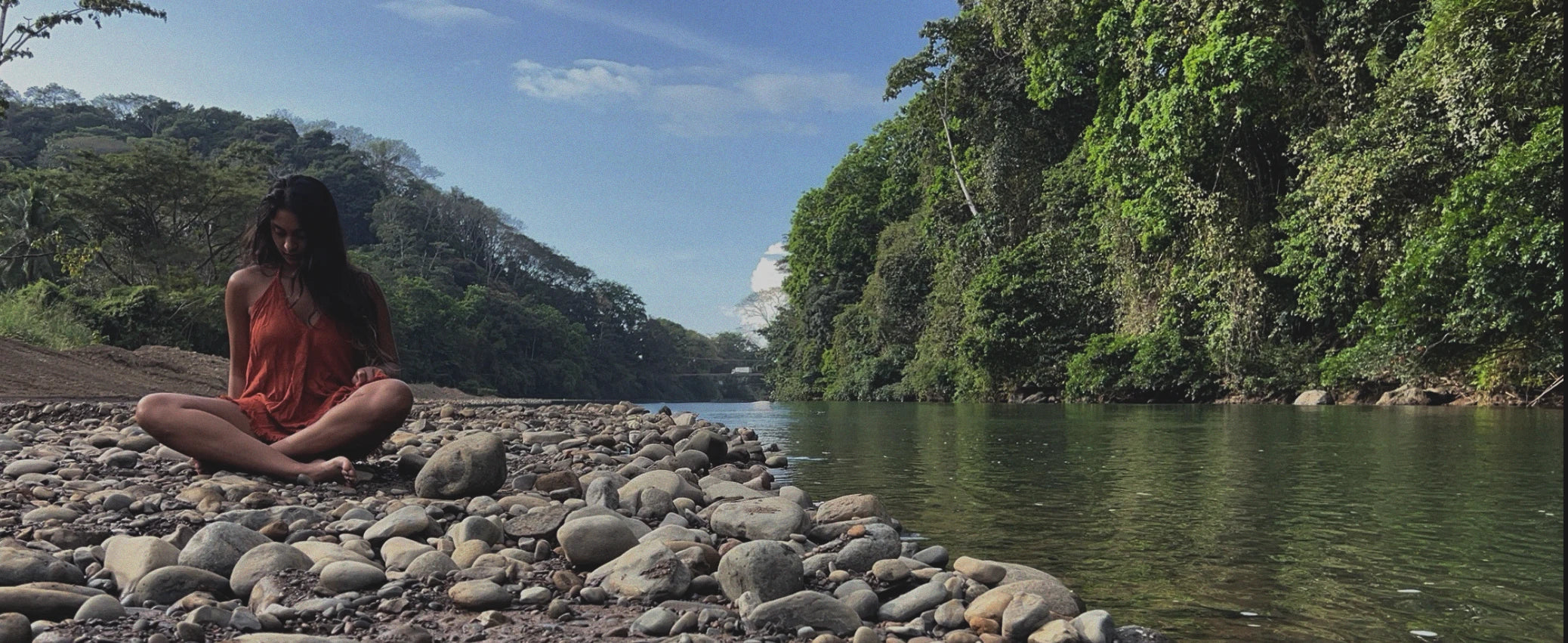 Kiseau founder meditating on rocks by a river with lush greenery and mountains in the background