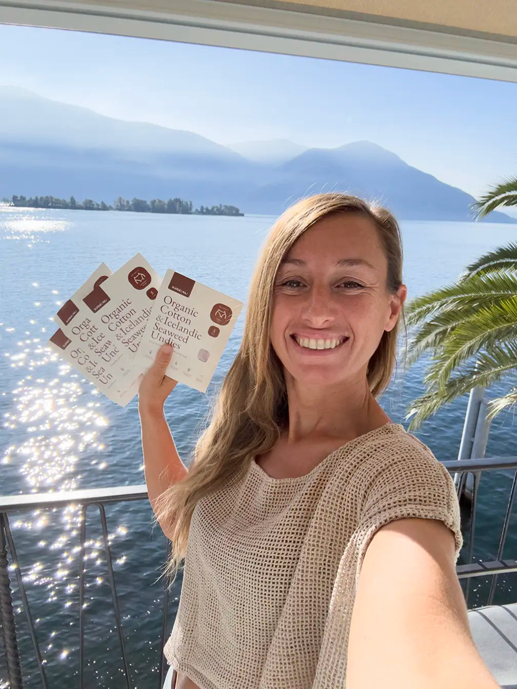 Customer Lucy holding Kiseau Organic Cotton & Icelandic Seaweed underwear boxes on balcony by the lake, sustainable and eco-friendly product.