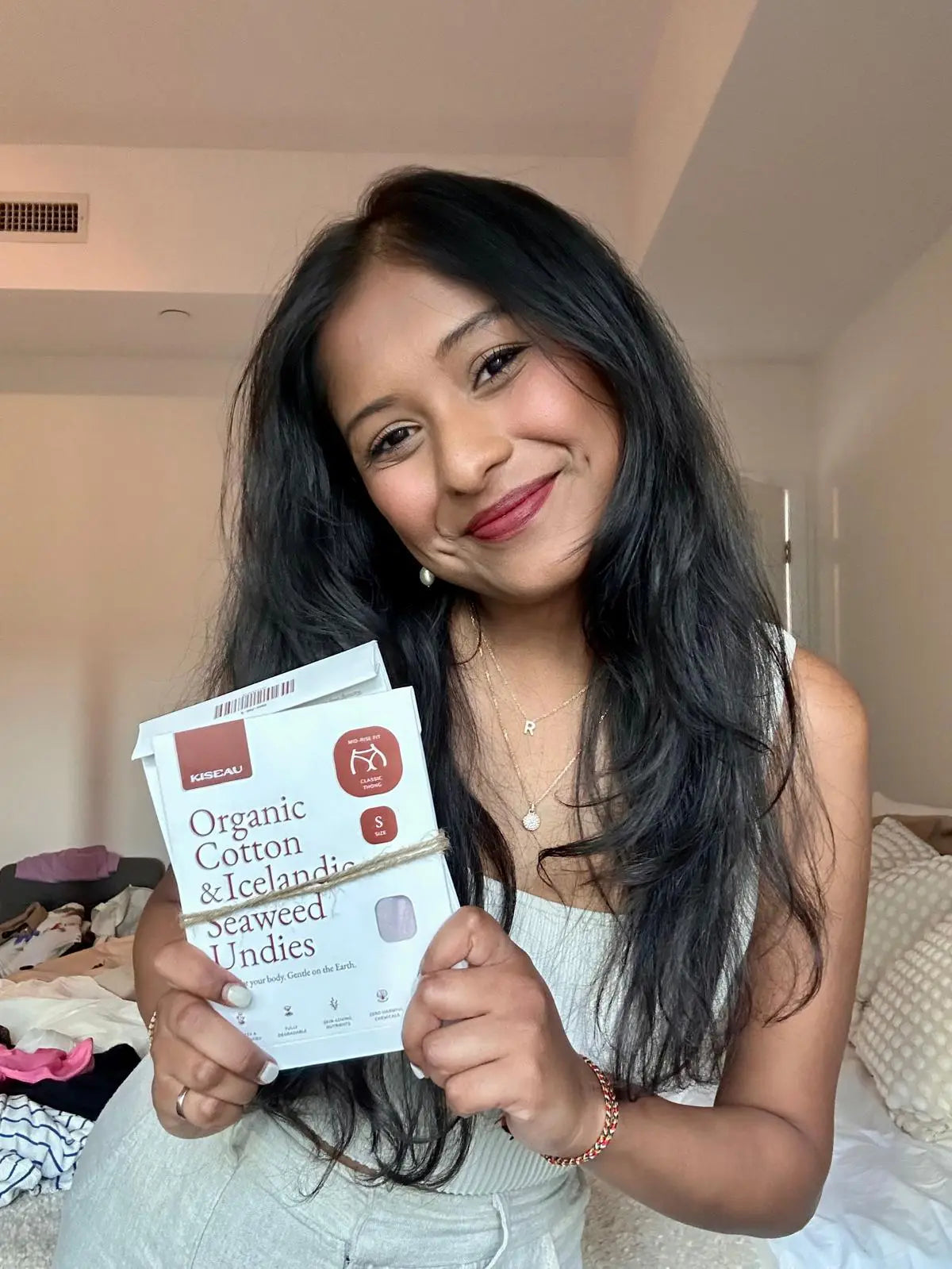 Customer Reka holding Kiseau Organic Cotton & Icelandic Seaweed underwear packaging, smiling indoors, sustainable and toxin-free design.