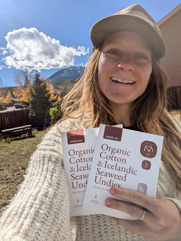 Customer smiling outdoors while holding two boxes of Kiseau Organic Cotton & Icelandic Seaweed Undies, sharing a positive review about comfort and natural materials.