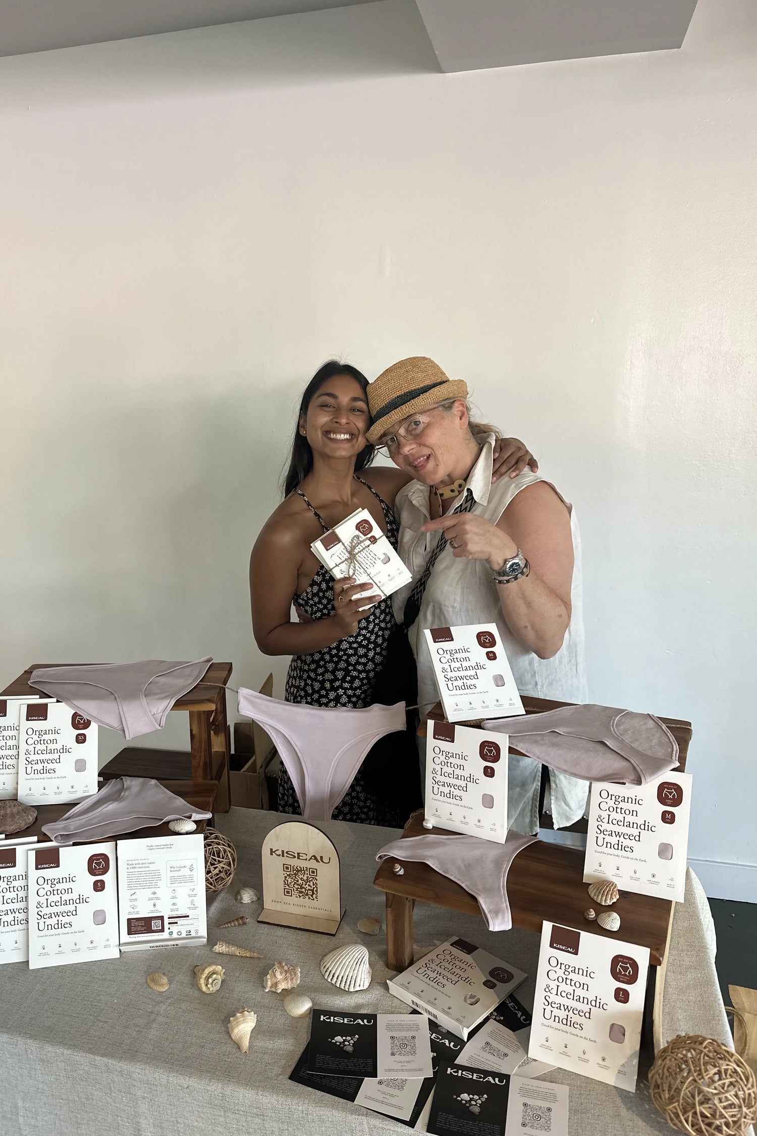 Two women smiling at a Kiseau market display featuring Organic Cotton & Icelandic Seaweed Undies, natural materials, and eco-conscious packaging.